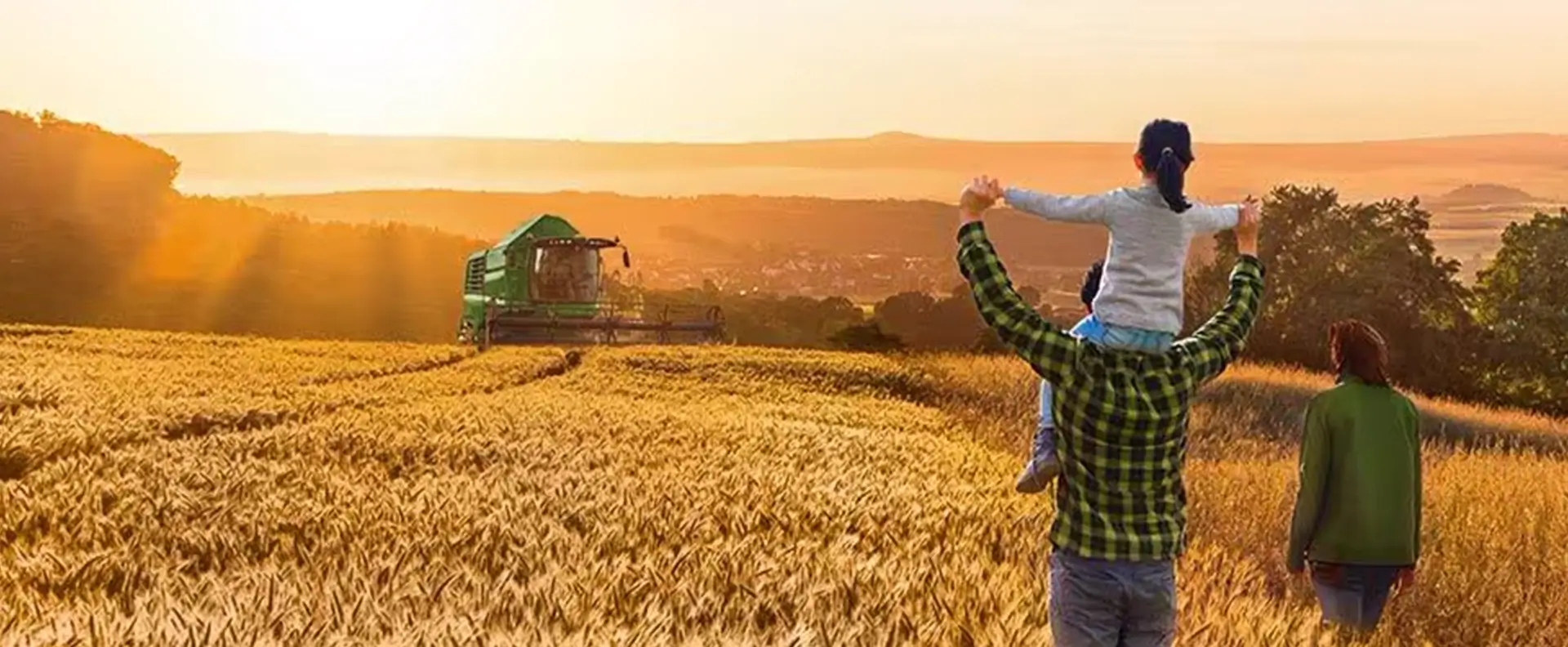 Familie schaut auf den Acker, Landmaschine und Sonnenuntergang im Hintergrund
