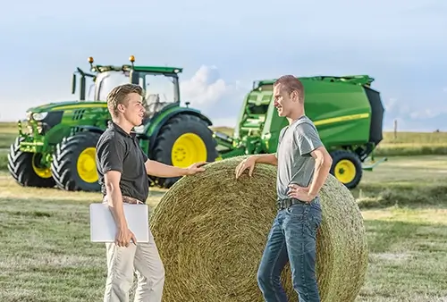 2 Männer am Strohballen im Gespräch, Landmaschine in Hintergrund